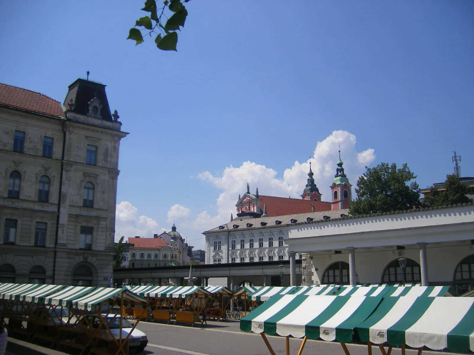 Open-air market stalls under green-and-white umbrellas at Ljubljana's Central Market, the cathedral towers behind